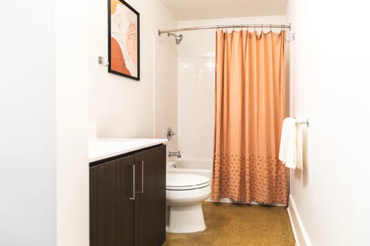 Detroit apartments for rent - image - a bathroom with a white toilet next to a shower with an orange shower curtain